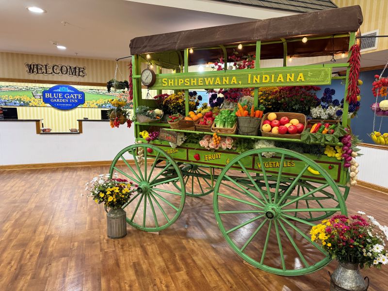 Cost of a Weekend in Shipshewana: What to Expect 1 A photo showing a hotel front desk in the background with a bright green wagon in the foreground full of colorful fruit and flower decorations.